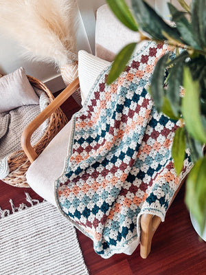 Crochet granny stitch blanket in rust, peach, teal and cream draped over a chair, seen from above
