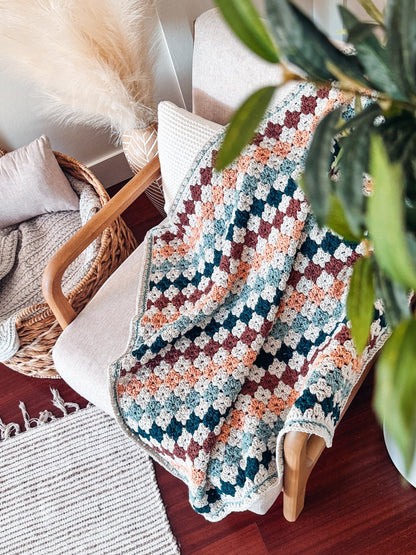 Crochet granny stitch blanket in rust, peach, teal and cream draped over a chair, seen from above
