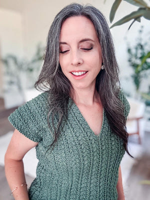 Green crochet top with short sleeves and V-neck, close up on a woman with long gray hair looking down and smiling