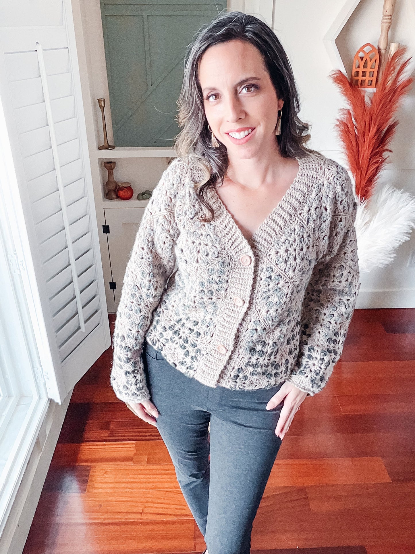 May include: A beige cardigan with a button closure and a delicate knit pattern. The cardigan is worn over gray pants.