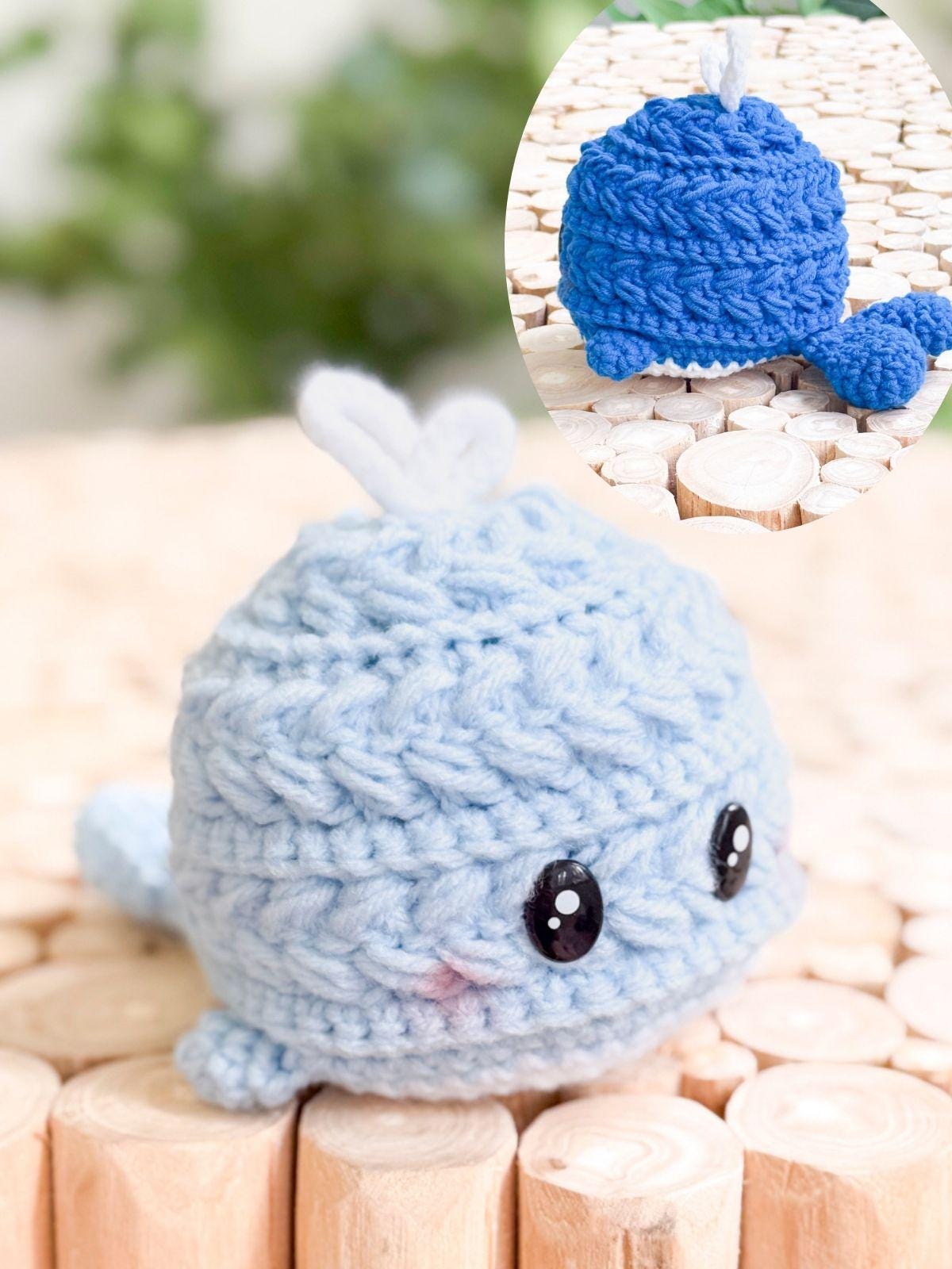 Crocheted plush whale in light blue with black eyes and a small tail, shown on a wooden surface; an inset shows a similar whale in dark blue from the back—a perfect handmade gift for ocean lovers.