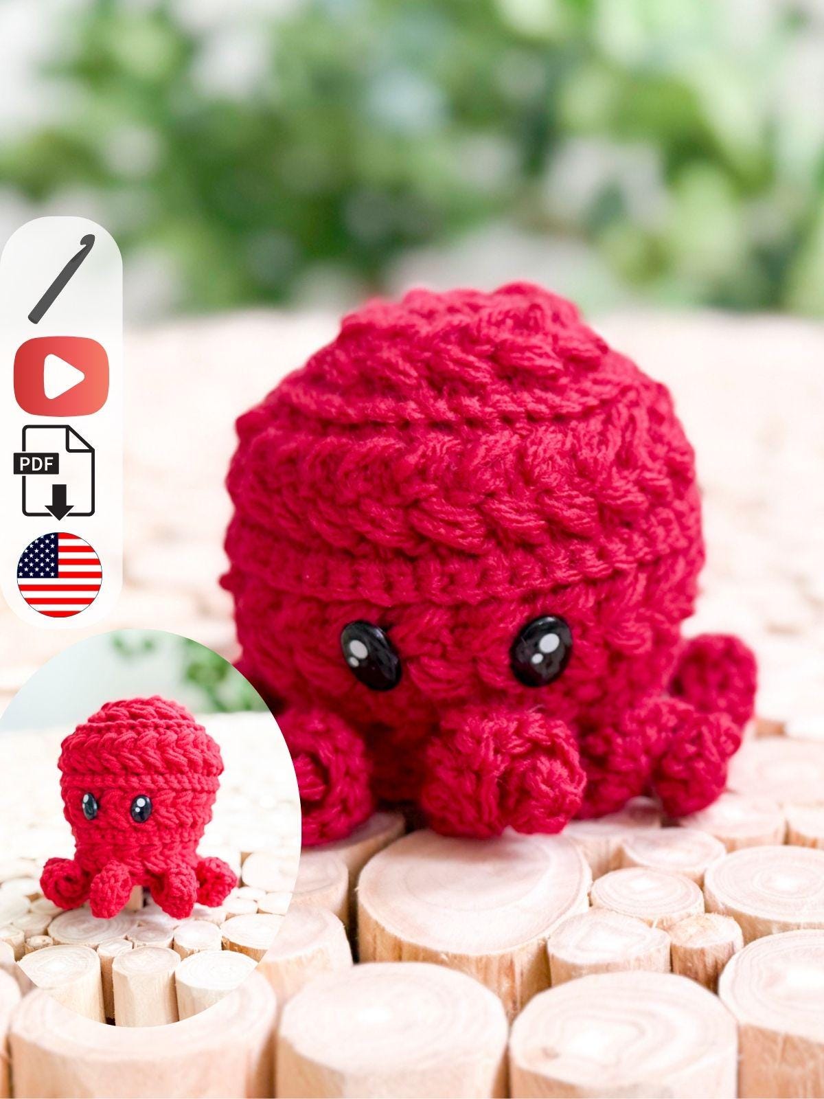 A small, red crocheted octopus with black eyes sits on a wooden surface, making a charming handmade gift. An inset shows a close-up of the same octopus. Icons for a video, PDF, and a USA flag appear on the left.