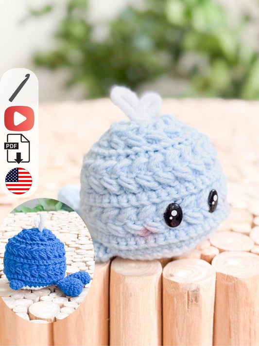 A small, crocheted blue whale plush toy with black eyes sits on a wooden surface—a charming handmade gift. An inset shows the back view and a tail detail.