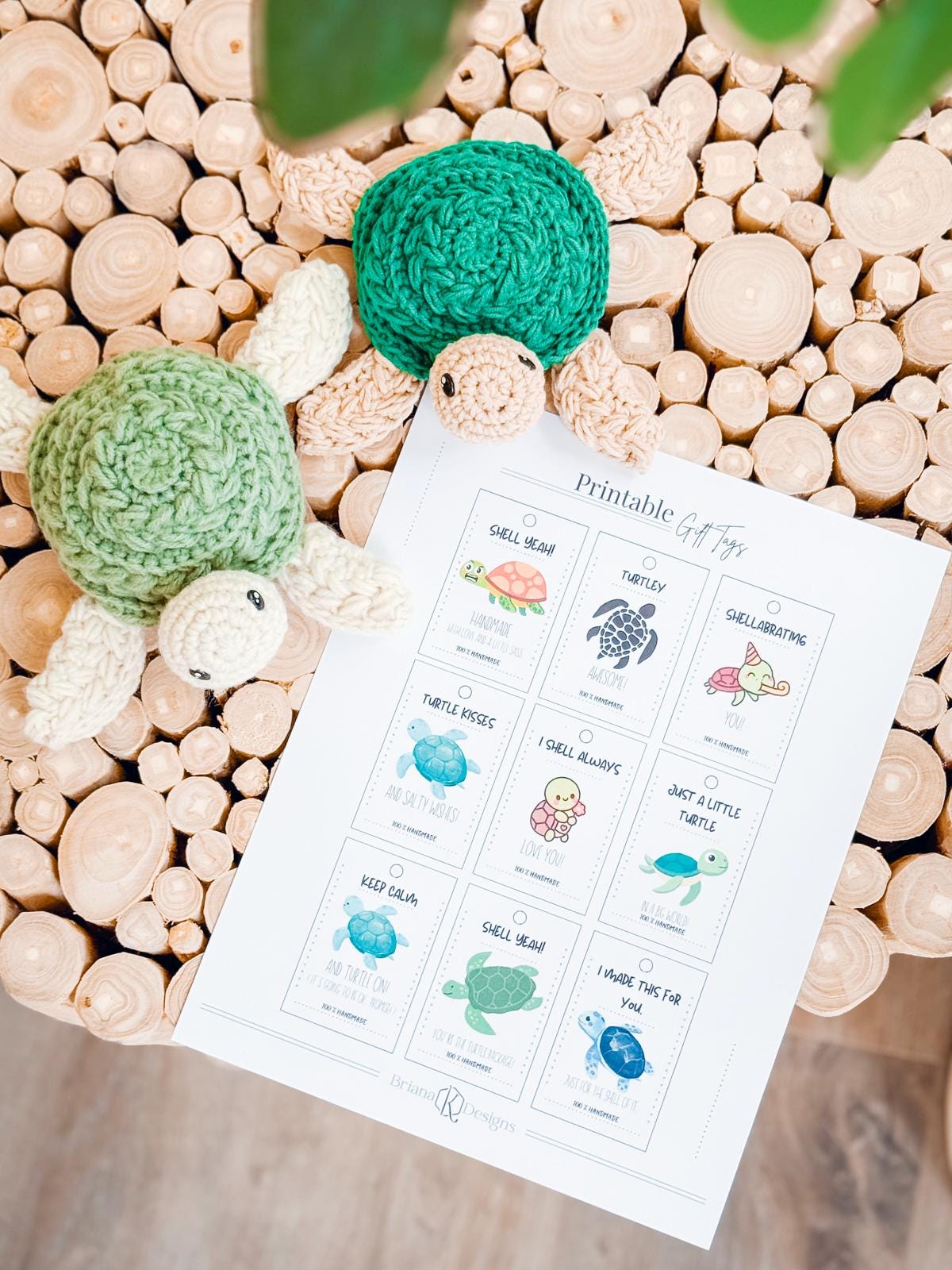 Two crocheted turtles rest on a circular wooden surface next to a sheet of printable turtle-themed gift tags—perfect for adding charm to any handmade gift with adorable illustrations and puns.