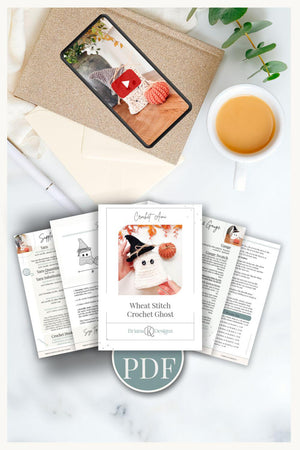 Flat lay of a crochet ghost pattern PDF, printed instructions, a cup of coffee, a plant, a phone with a crochet ghost photo, and an envelope—perfect inspiration for your next handmade gift.