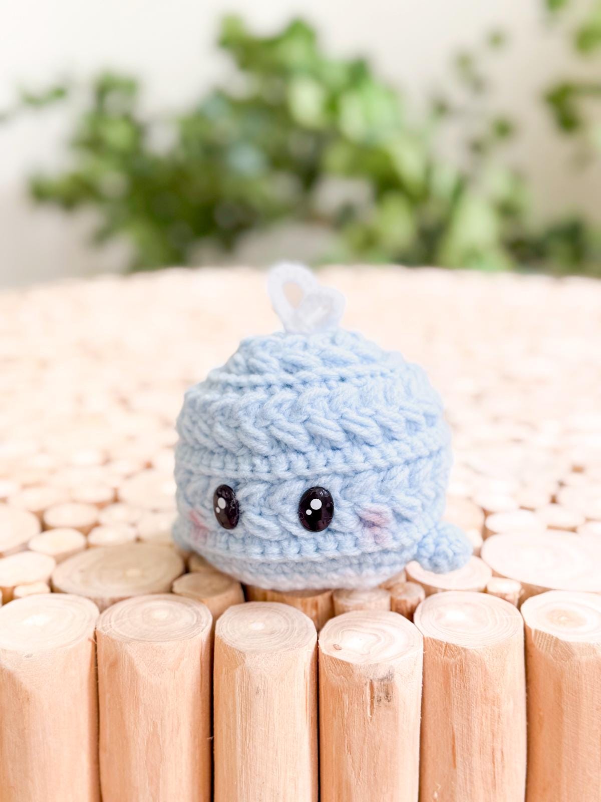 A small, crocheted blue whale plush with black eyes sits on a light wooden surface—perfect as a charming handmade gift from an easy crochet pattern.