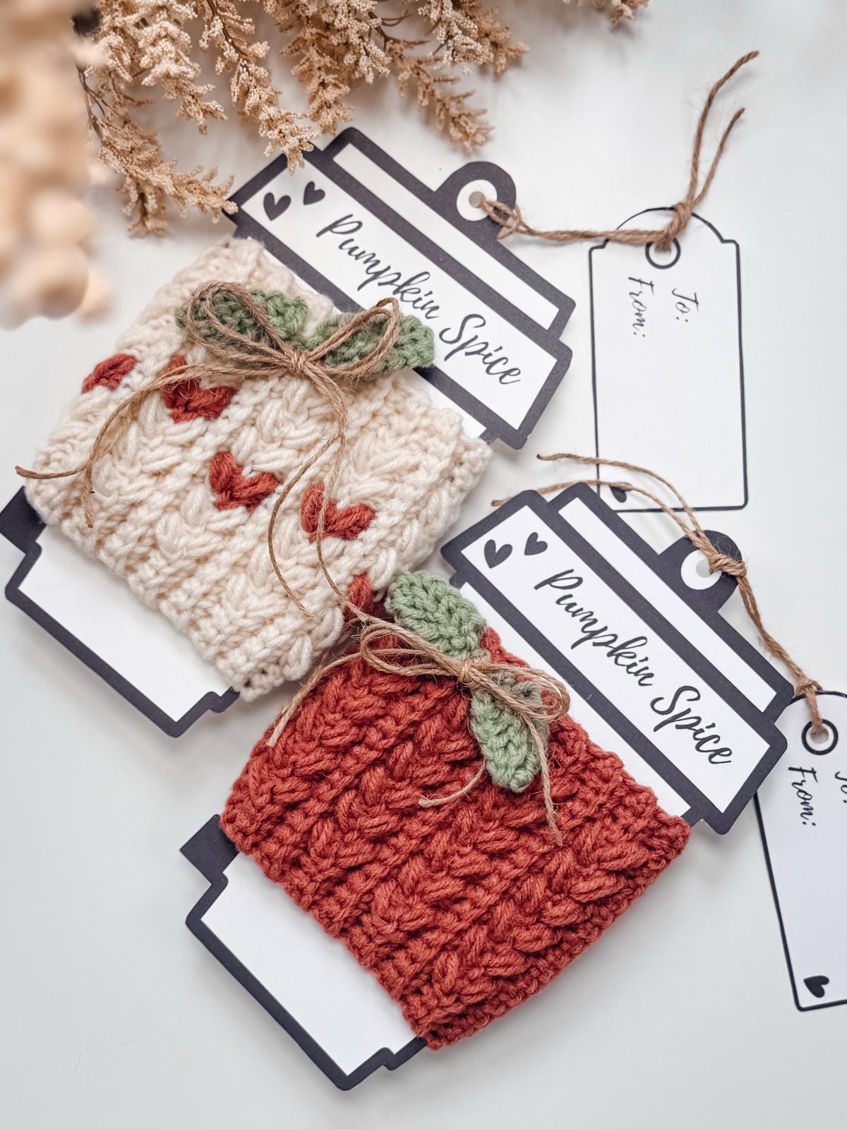 A flat lay of a crochet pattern PDF, printed pages, a phone showing a crochet video, an envelope, unique jewellery pieces, and a cup of tea on a light surface—perfect inspiration for your next handmade gift.