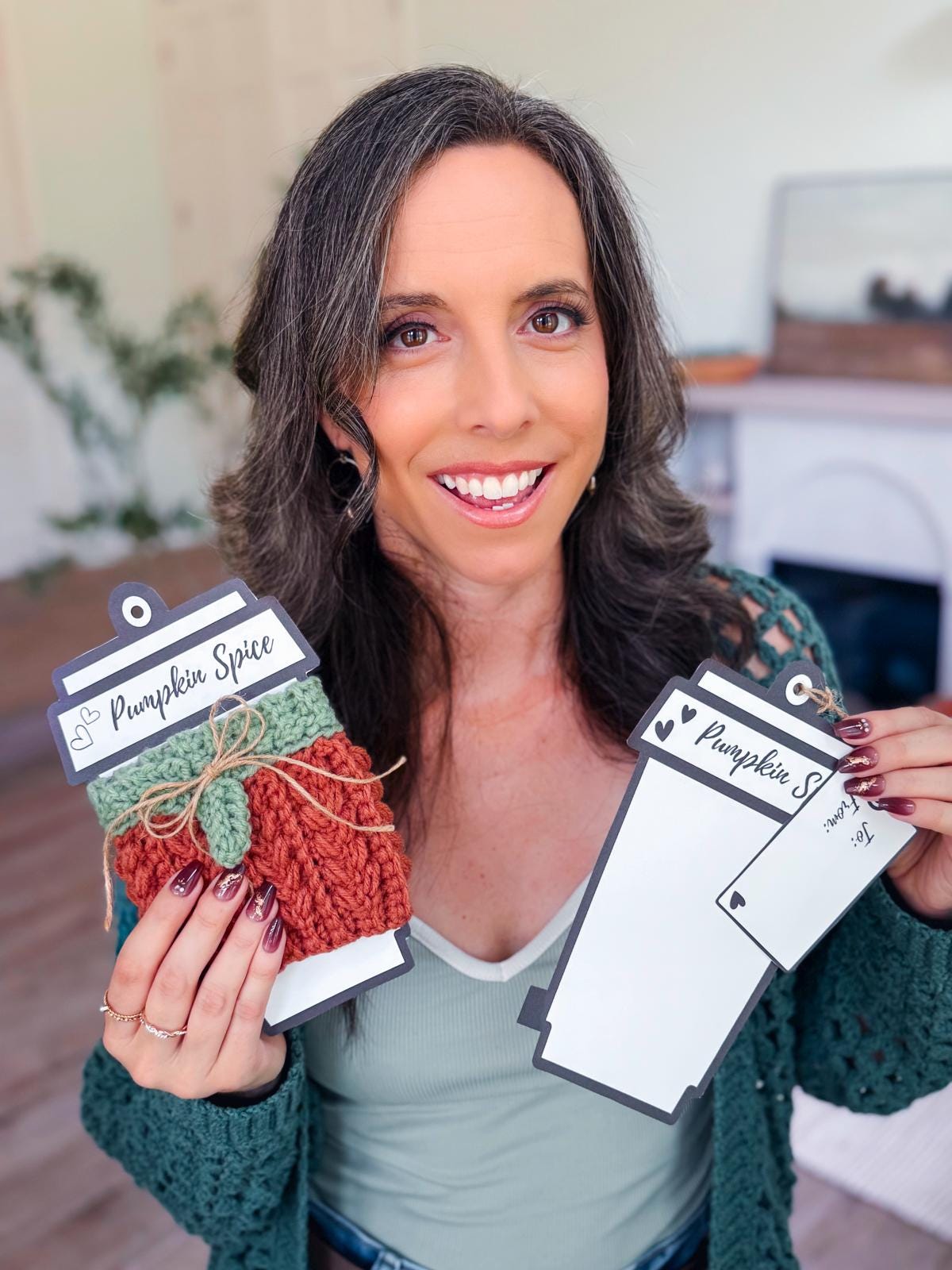 A woman smiles at the camera while holding a pumpkin spice-themed handmade gift with a crochet cozy and a blank pumpkin spice tag.