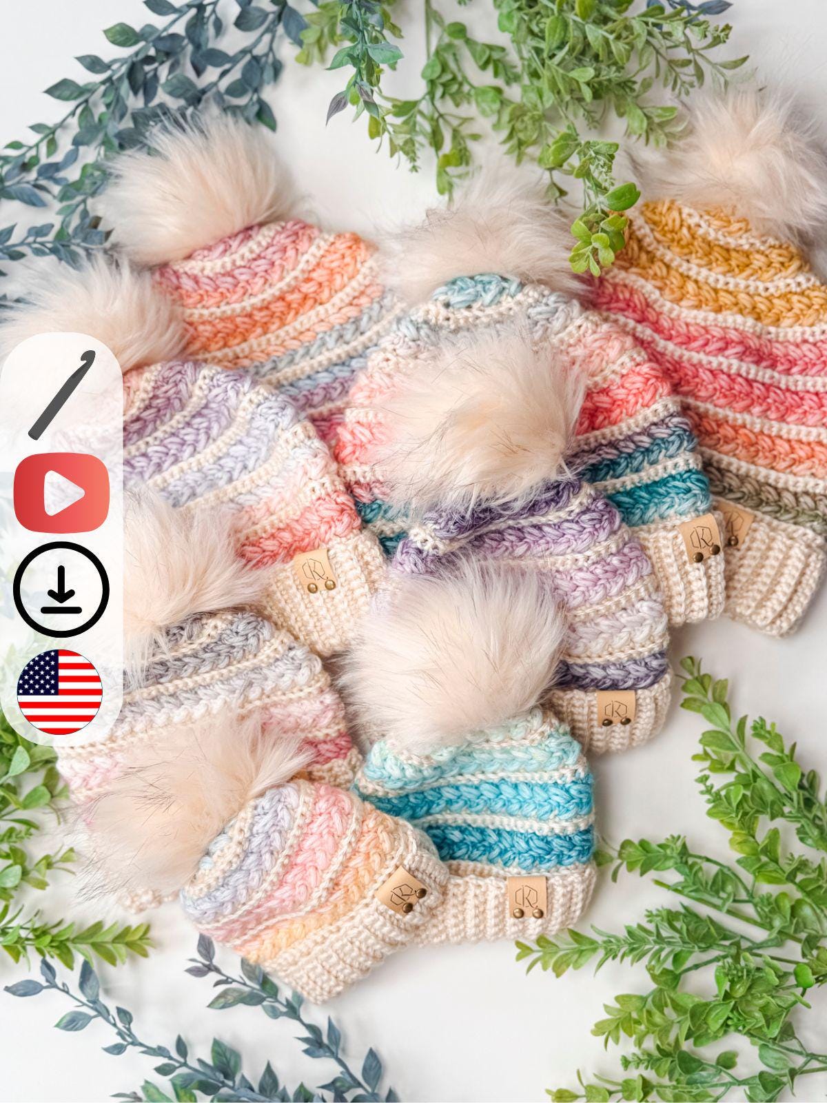 Seven colorful, crocheted beanies with faux fur pom-poms are arranged on a white surface, surrounded by green leafy branches—perfect as a handmade gift for those who love cozy style and thoughtful touches.