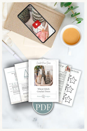 A flat lay of a crochet pattern PDF titled "Wheat Stitch Crochet Trees," printed pages, a cup of tea, an envelope, and a tablet displaying a crochet video—perfect inspiration for crafting a handmade gift.