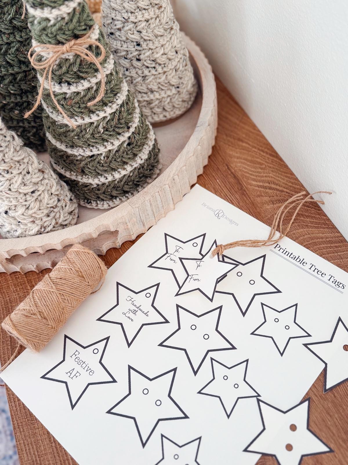 A sheet of printable star-shaped tree tags, a spool of twine, and crocheted decorative trees on a wooden tray atop a wooden surface—perfect accents for a handmade gift or thoughtful touch to vintage clothes.