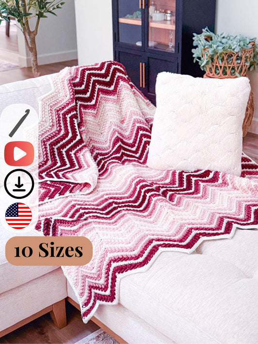 Red and white chevron crochet blanket draped over a beige sectional sofa with a white textured pillow, near a black cabinet and potted plant. Perfect as a handmade gift. Text overlay mentions "10 Sizes" and icons.