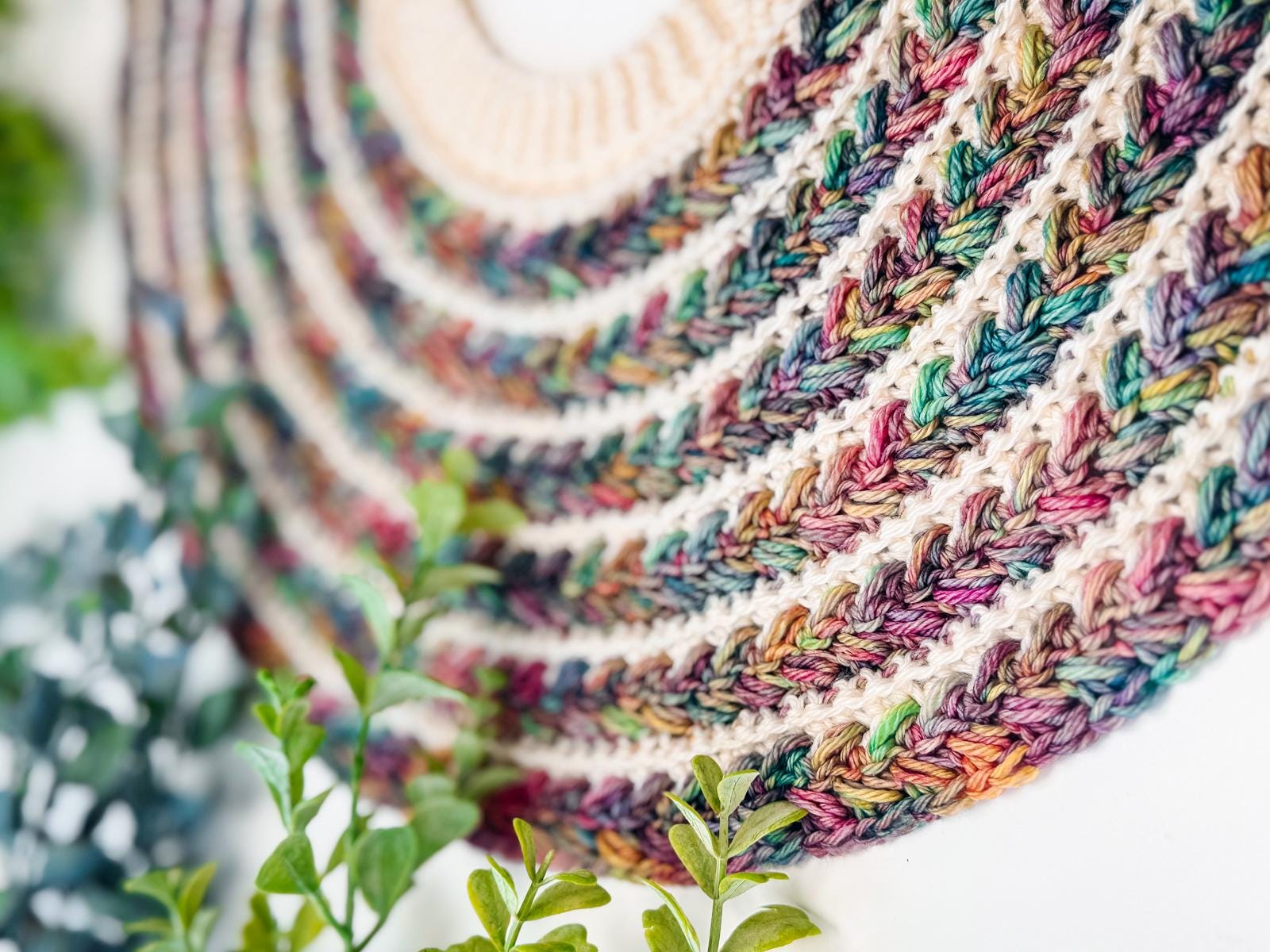 Close-up of a multicolored crocheted pattern arranged in concentric circles, with green plants in the foreground—perfect inspiration for crochet sweaters or a thoughtful handmade gift.