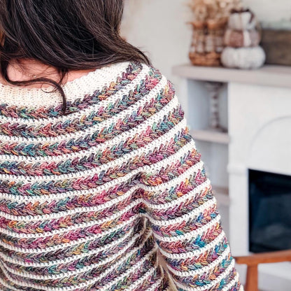 Back shoulder close-up of a multicolor and cream striped crochet sweater with braided texture near a fireplace