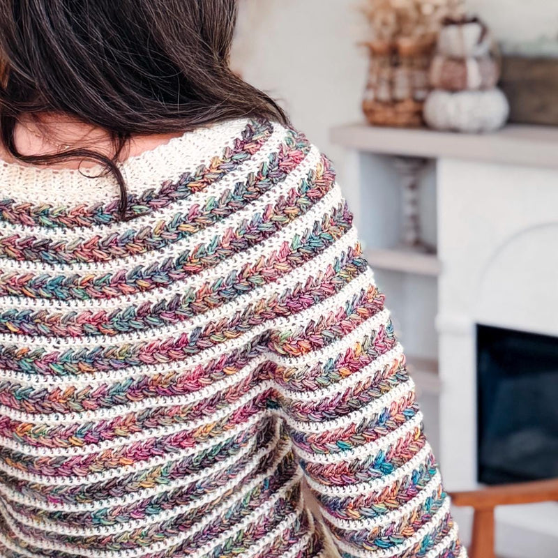 Back shoulder close-up of a multicolor and cream striped crochet sweater with braided texture near a fireplace
