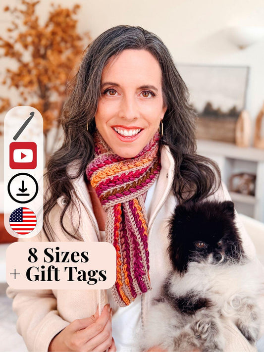 Woman with long dark hair wearing a multicolored crochet scarf, holding a small black and white dog. Text advertises knitting pattern in 8 sizes plus gift tags—perfect for a handmade gift. Icons for YouTube and US flag are shown.
