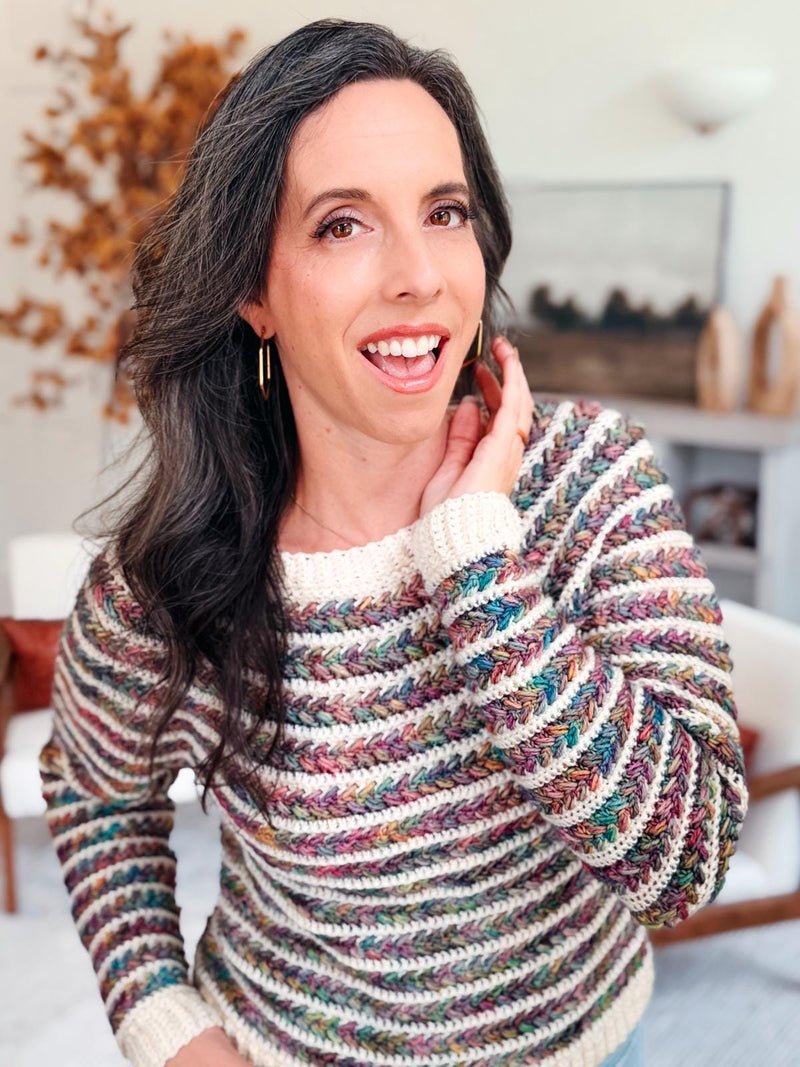 Multicolor striped crochet sweater with cream ribbed cuffs and neckline worn by a laughing woman indoors