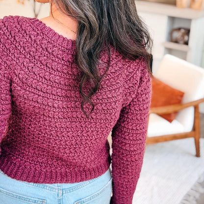 Back view of a plum crochet sweater with textured braided rows and ribbed hem worn with light jeans