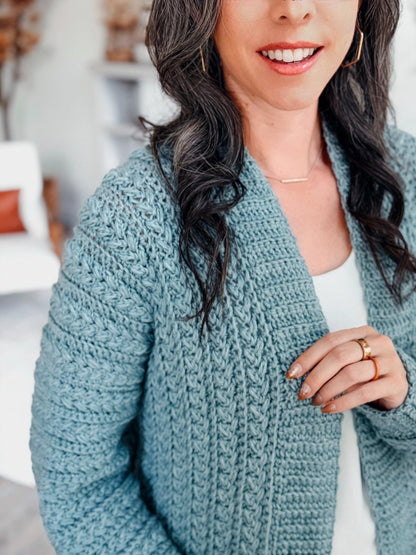 Close-up of sage blue crochet cardigan showing braided stitch texture and ribbed collar on a woman