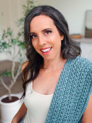 Close-up of blue crochet cardigan panel with braided wheat texture draped over a smiling woman's shoulder