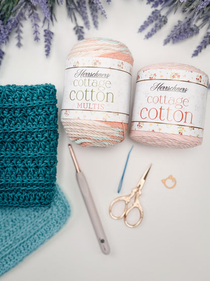 Teal crochet washcloths beside two cotton yarn cakes, a crochet hook, gold scissors, and a stitch marker