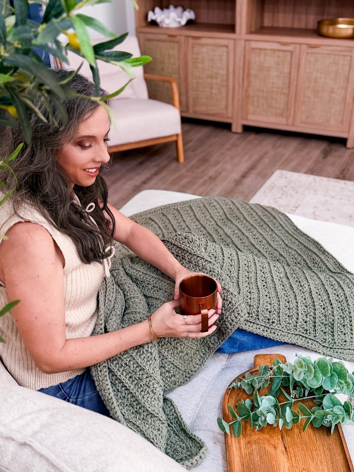 Sage green crochet throw blanket across the lap on a couch
