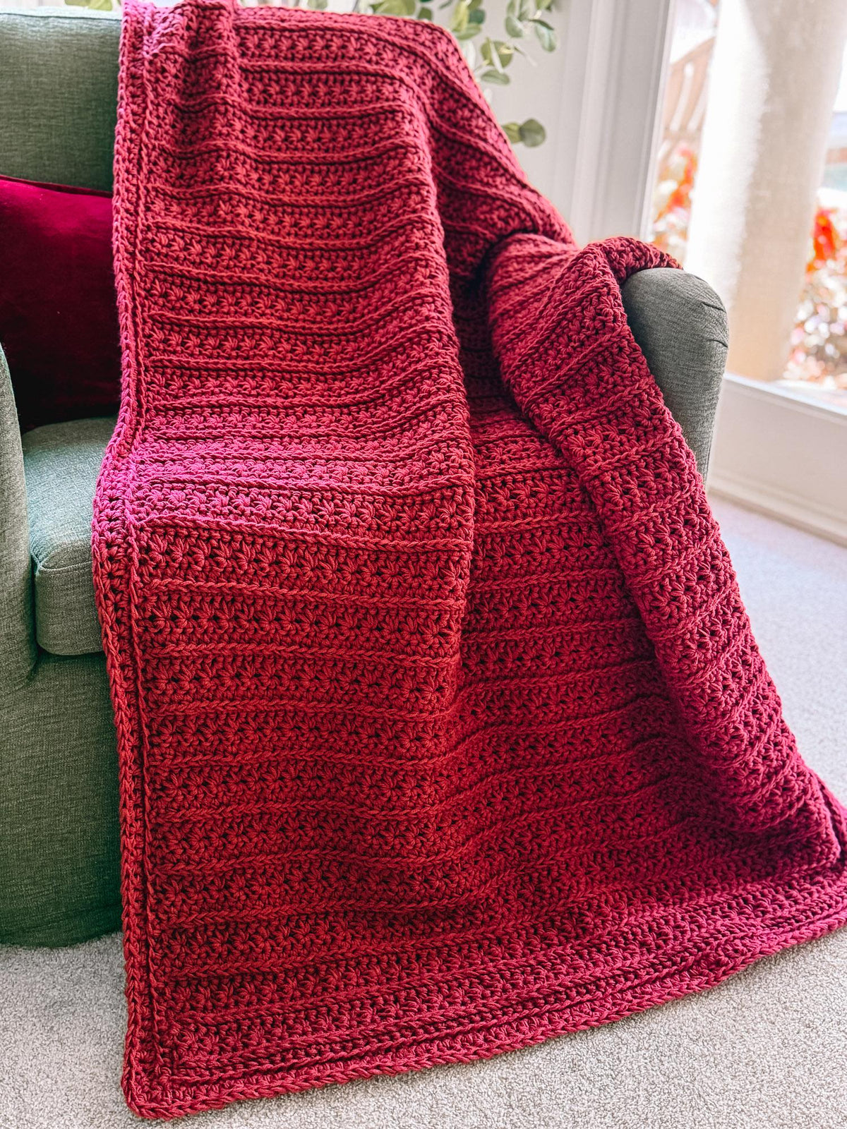 Deep red Petal Loop Stitch crochet blanket hanging over a chair