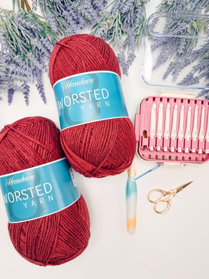 Worsted weight yarn in deep red with crochet hooks and scissors for the Petal Loop Stitch blanket