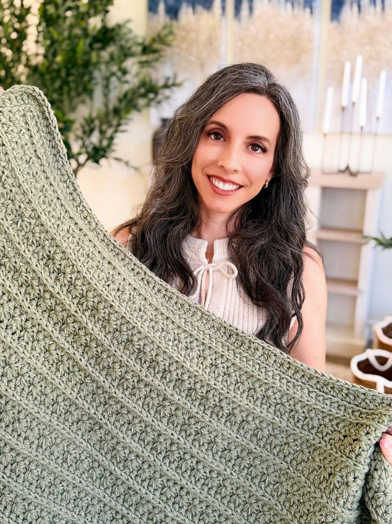 Holding up the sage green Petal Loop Stitch crochet blanket