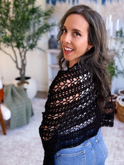 Willow Mesh Wrap crochet pattern: black lacy crochet wrap draped over the shoulders of a smiling woman in jeans, looking back in a bright living room
