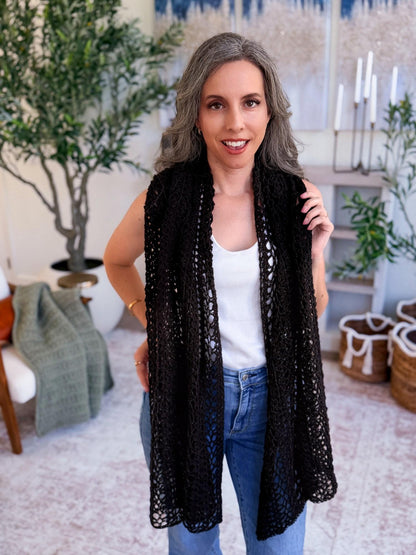 Black lacy crochet wrap hanging long like a scarf over a woman's white top and jeans in a living room