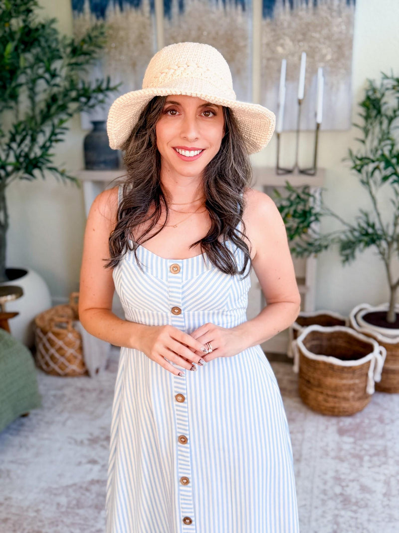Cream crochet sun hat worn by a smiling woman standing in a striped sundress