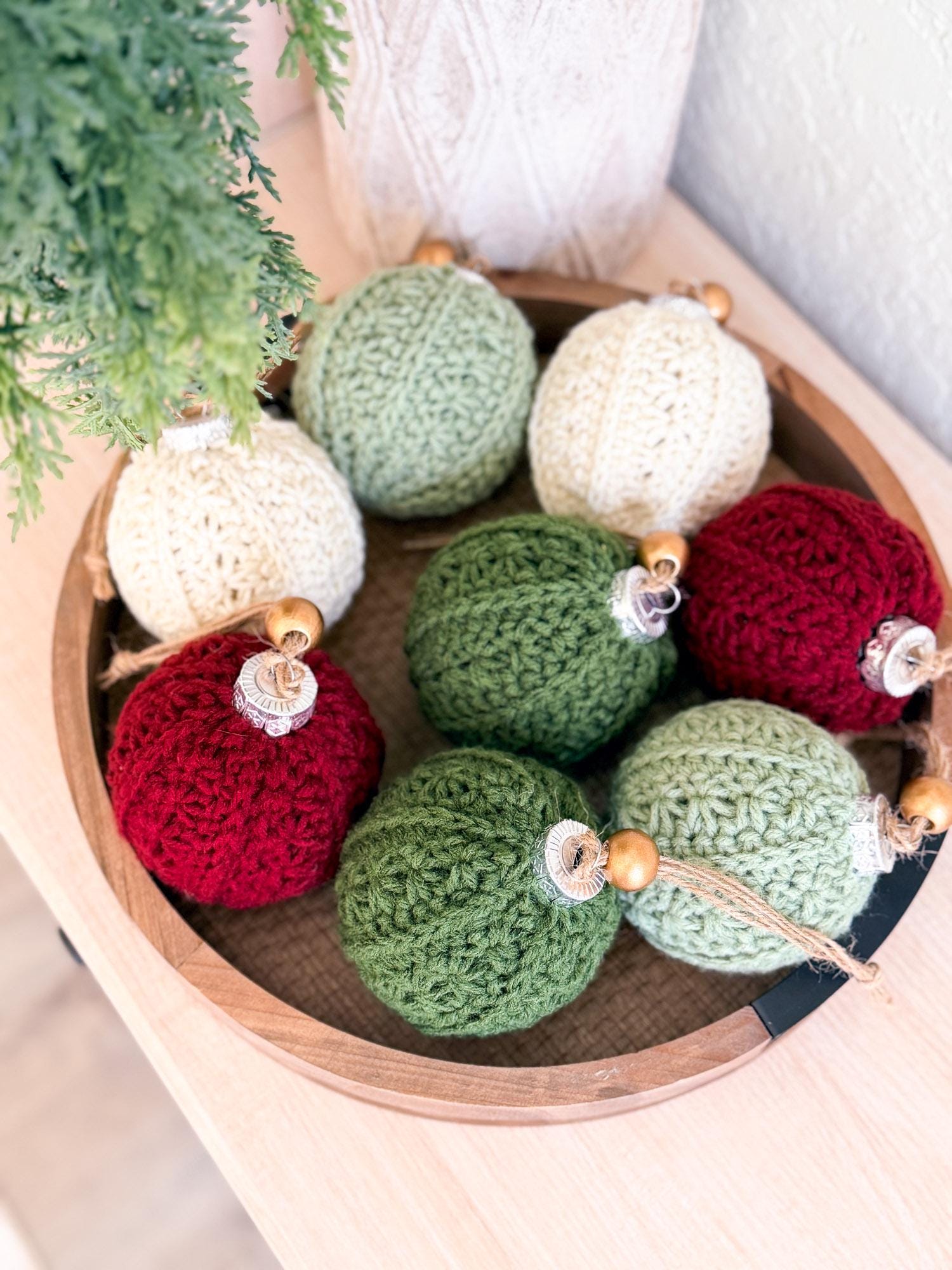 Crocheted Christmas ornaments in red, green, and white on a wooden tray.