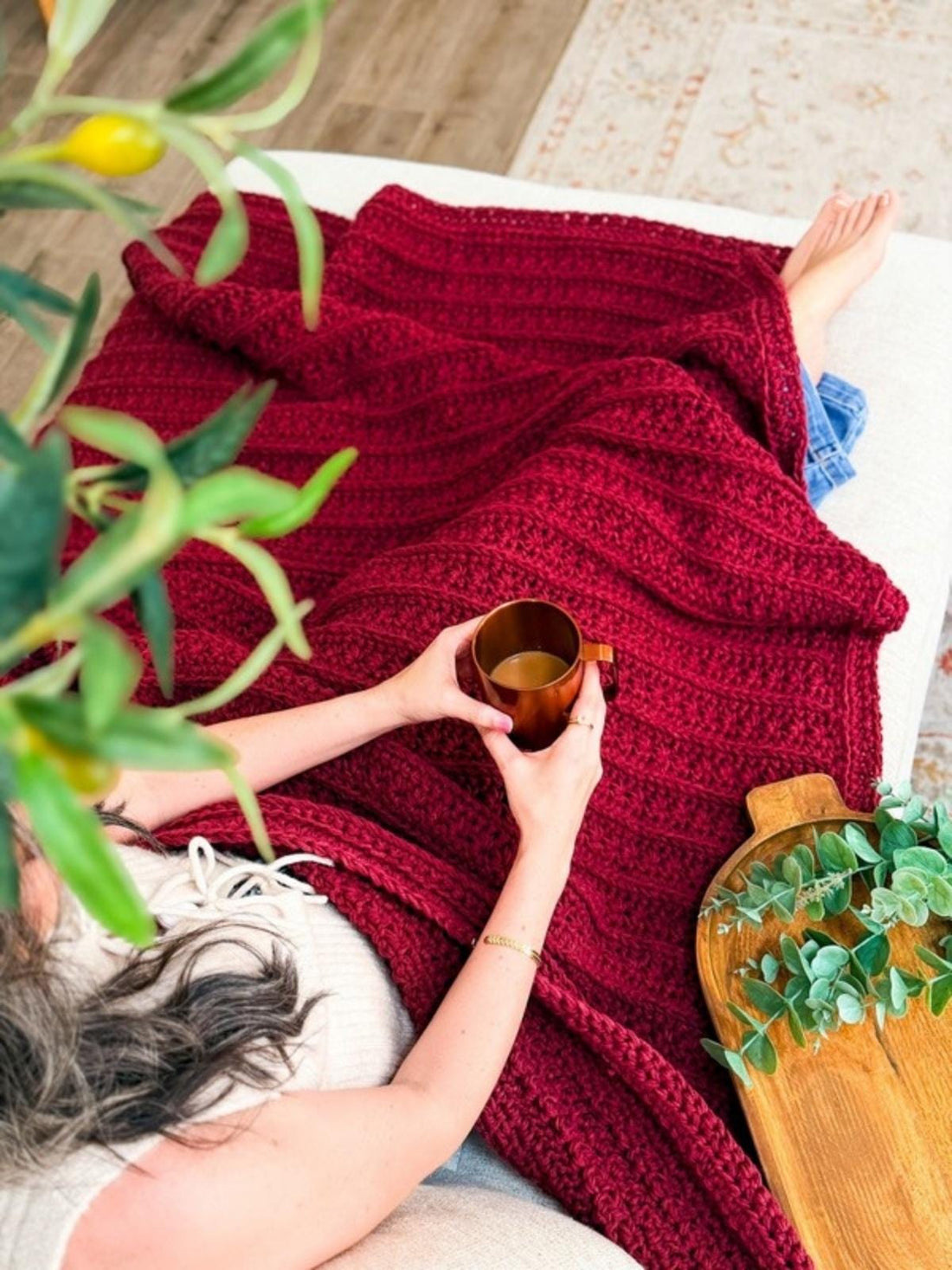 Petal Loop Stitch crochet blanket in deep red draped across a lap with a mug of coffee