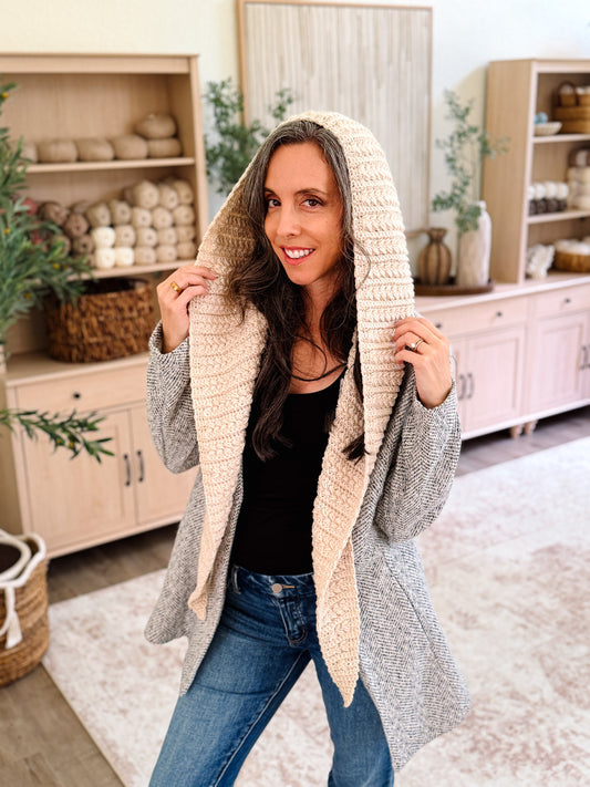 Woman wearing the cream Wheat Stitch crochet hooded scarf with the hood up over a gray coat
